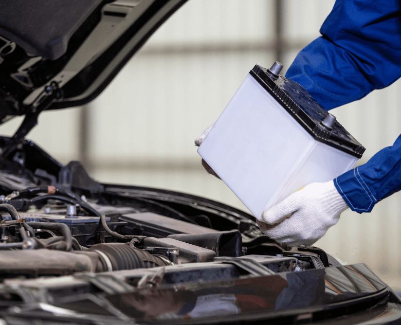 Technician lifting a car battery out of an engine bay