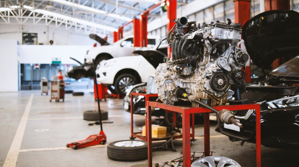 Engine on a stand in a service bay, with vehicles raised on lifts behind it